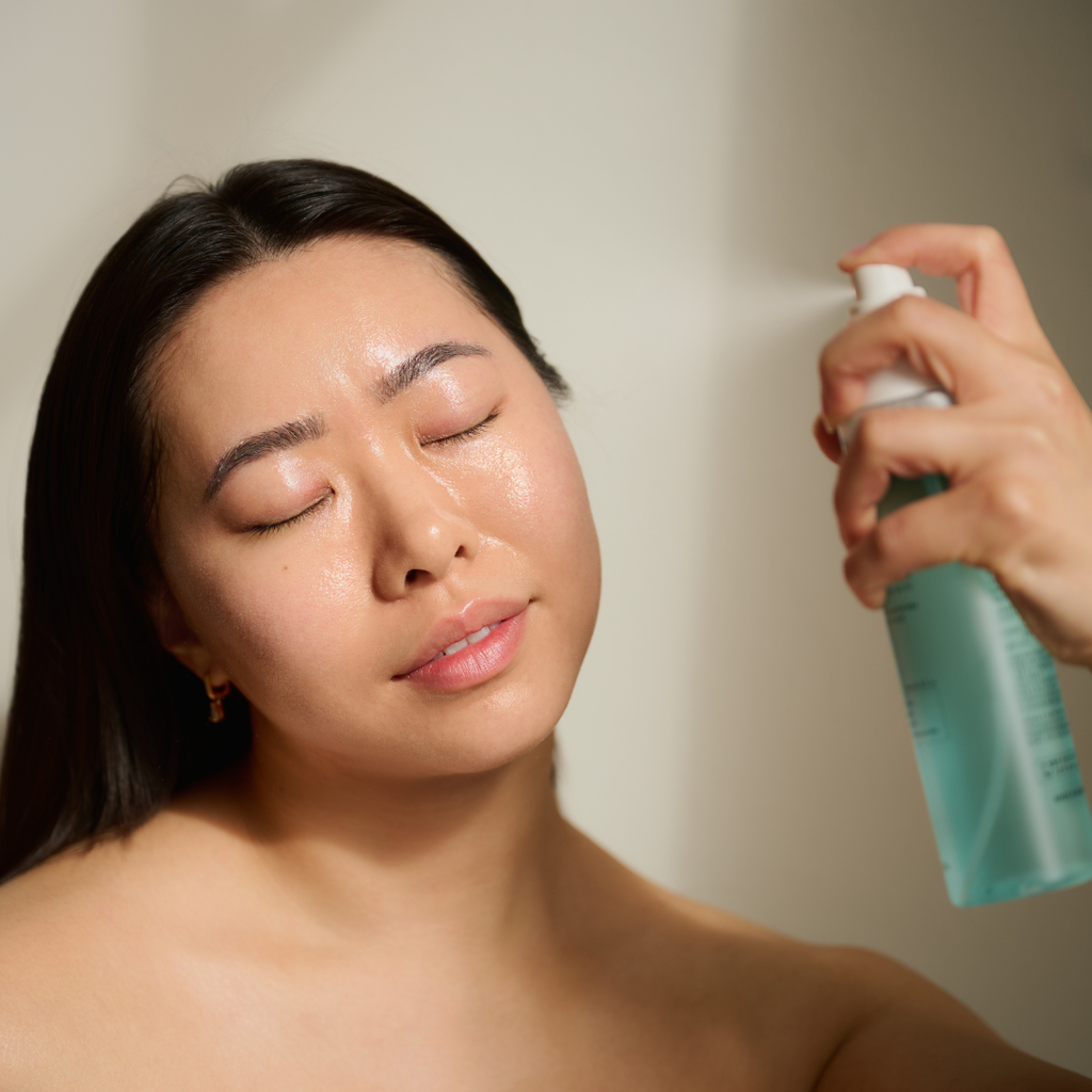 Woman with glowing skin misting Thesera Hydroglow Cell Ampoule Mist onto her face with eyes closed — hydrating facial mist with hyaluronic acid for dehydrated and sensitive skin
