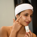 Woman applying Dermathod Toning Peel Refiner to her cheek, wearing a white headband, nighttime skincare routine for hyperpigmentation and uneven skin tone