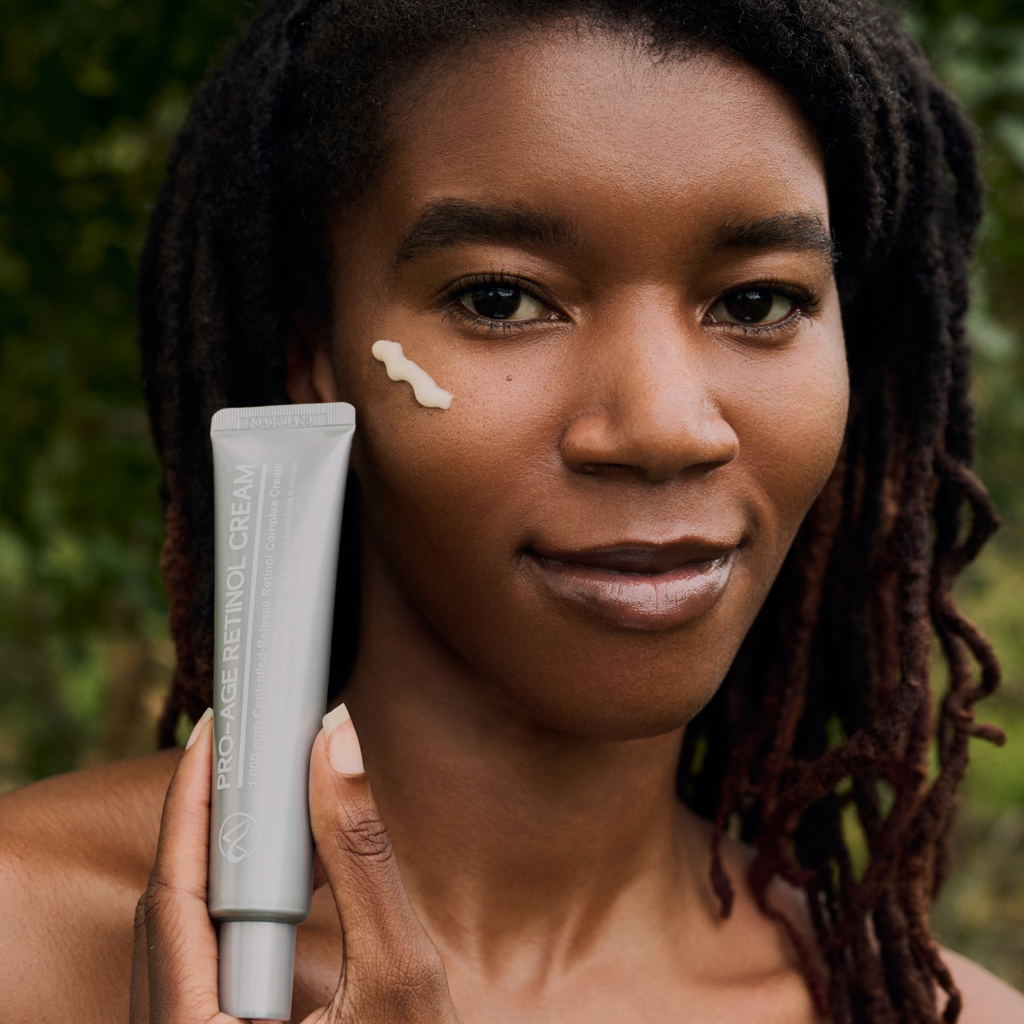 Woman with glowing skin holding Pfect-A ProAge Controlled Release Retinol Cream tube with cream applied to her cheek — gentle overnight retinol treatment for aging and uneven skin tone
